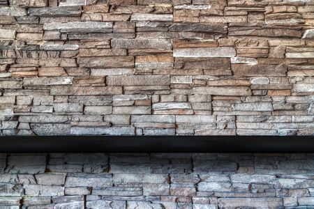 Stone brick wall background with empty black wooded shelf  for mock up display or montage of product design and copy space.の写真素材