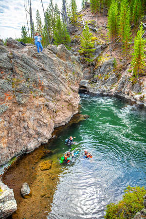 Wyoming, USA - Aug. 24, 2019: Group of scuba divers explore Firehole River in Yellowstone National Park, Wyoming, USA, while a tourist takes pictures on top of a rock. The river flows through several significant geyser basins in Yellowstone National Park.のeditorial素材