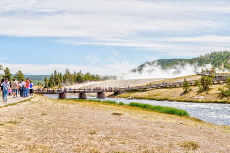 Wyoming, USA - Aug. 24, 2019: Visitors approach the footbridge to Grand Prismatic Spring in Yellowstone National Park with steam rising from the thermal landscape of Excelsior Geyser in the background.のeditorial素材