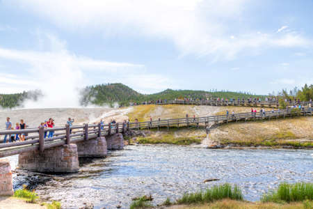 Wyoming, USA - Aug. 24, 2019: Visitors approach the footbridge to Grand Prismatic Spring in Yellowstone National Park with steam rising from the thermal landscape of Excelsior Geyser in the background.のeditorial素材