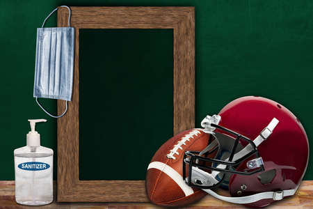 COVID-19 new normal sports concept in a classroom setting showing framed chalkboard with copy space and American football and helmet on wooden table.の写真素材