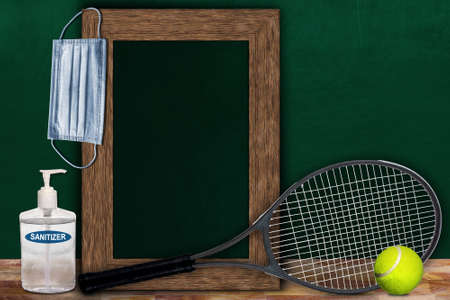 COVID-19 new normal sports concept in a classroom setting showing framed chalkboard with copy space and tennis racket and ball on wooden table.の写真素材