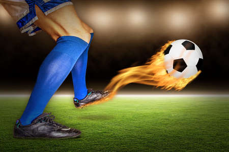 Soccer player kicking a fiery flaming football in flight at a stadium.の写真素材