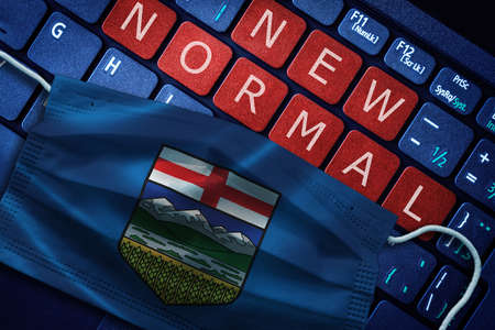 COVID-19 coronavirus new normal concept in the Canadian province of Alberta as shown by Alberta flag on face mask with New Normal on laptop red alert keyboard buttons.の写真素材