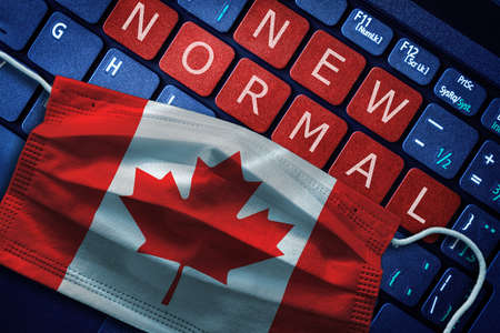 COVID-19 coronavirus new normal concept in Canada as shown by Canadian flag on face mask with New Normal on laptop red alert keyboard buttons.の写真素材