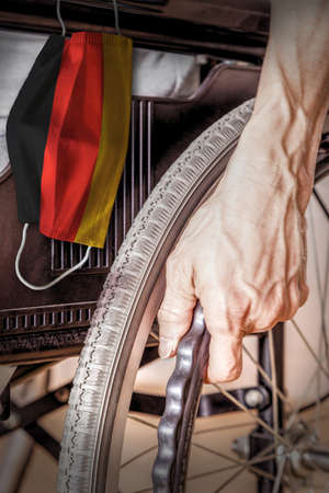 Elderly person in wheelchair at Germany nursing home with hanging German flag face mask. Concept of Covid-19 coronavirus outbreak in nursing care homes or elderly retirement facilities.の写真素材