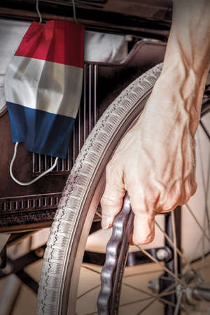 Elderly person in wheelchair at France nursing home with hanging French flag face mask. Concept of Covid-19 coronavirus outbreak in nursing care homes or elderly retirement facilities.の写真素材