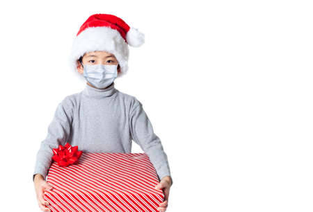LIttle boy receiving Xmas gift during Covid Christmas wearing Santa hat and face mask due to pandemic, isolated on white background with copy space.の写真素材