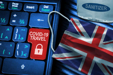 UK COVID-19 coronavirus travel restrictions concept showing red button warning on keyboard with British flag face mask and hand sanitizer. New normal in global travel.の写真素材