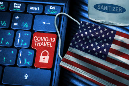 US COVID-19 coronavirus travel restrictions concept showing red button warning on keyboard with American flag face mask and hand sanitizer. New normal in global travel.の写真素材