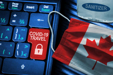Canada COVID-19 coronavirus travel restrictions concept showing red button warning on keyboard with Canadian flag face mask and hand sanitizer. New normal in global travel.の写真素材