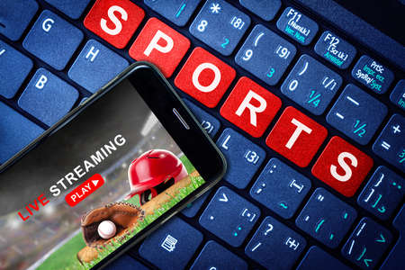 Sports Live streaming concept showing baseball game broadcast on smartphone with laptop high tech background. Accessible on demand digital content is the future of sports broadcasting.の写真素材