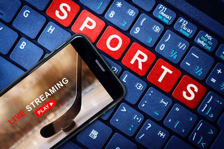 Sports Live streaming concept showing ice hockey game broadcast on smartphone with laptop high tech background. Accessible on demand digital content is the future of sports broadcasting.の写真素材
