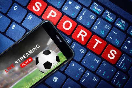 Sports Live streaming concept showing Soccer or football game broadcast on smartphone with laptop high tech background. Accessible on demand digital content is the future of sports broadcasting.の写真素材