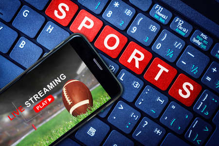 Sports Live streaming concept showing Football game broadcast on smartphone with laptop high tech background. Accessible on demand digital content is the future of sports broadcasting.の写真素材