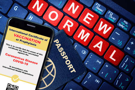 Smartphone digital app certification on passport as proof of vaccination for new normal travel during pandemic. Keyboard background with red New Normal text.の写真素材