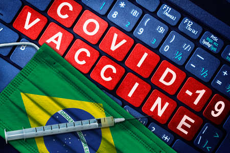 COVID-19 immunization in Brazil showing syringe and face mask with Brazilian flag and vaccine message on computer keyboard. Concept of Covid vaccination in the countryの写真素材