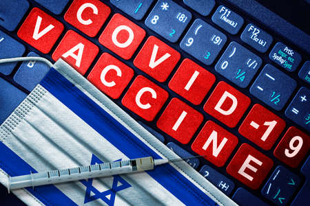 COVID-19 immunization in Israel showing syringe and face mask with Israeli flag and vaccine message on computer keyboard. Concept of Covid vaccination in the countryの写真素材