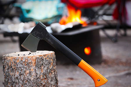 Axe stuck on tree stump with firewood burning in camping fire pit in the background. Outdoor camping in Banff National Park. Selective focus on foreground.の写真素材