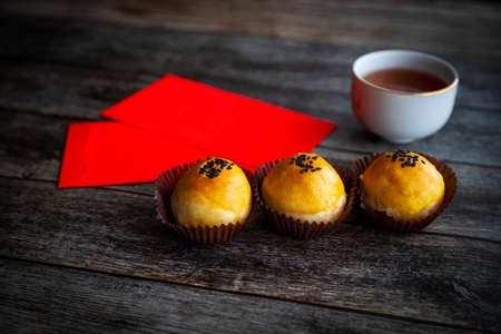 Traditional Chinese New Year pastries baked with fluffy dough and filled with salted egg yolk and sweet paste. Chinese lucky money red packets and tea in background on rustic wooden table.の写真素材
