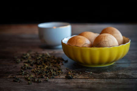 Hard boiled Chinese marble spiced tea eggs on rustic wooden table with tea leaves and cup of Chinese tea in background.の写真素材