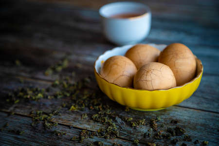 Hard boiled Chinese marble spiced tea eggs on rustic wooden table with tea leaves and cup of Chinese tea in background.の写真素材