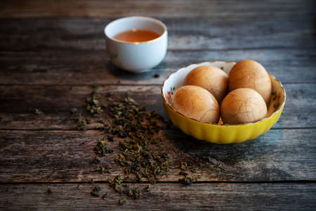 Hard boiled Chinese marble spiced tea eggs on rustic wooden table with tea leaves and cup of Chinese tea in background.の写真素材