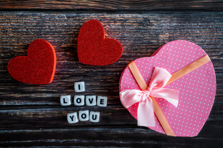 Pink heart shaped Valentine's Day gift box on wooden table with I Love You text and copy space.