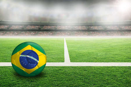 Football in brightly lit outdoor stadium with painted flag of Brazil. Focus on foreground and soccer ball with shallow depth of field on background and copy space.の写真素材