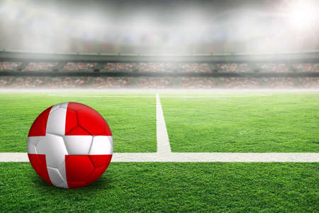 Football in brightly lit outdoor stadium with painted flag of Denmark. Focus on foreground and soccer ball with shallow depth of field on background and copy space.の写真素材