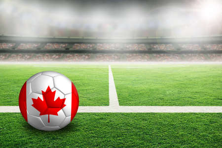 Football in brightly lit outdoor stadium with painted flag of Canada. Focus on foreground and soccer ball with shallow depth of field on background and copy space.の写真素材