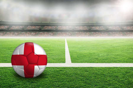 Football in brightly lit outdoor stadium with painted flag of England. Focus on foreground and soccer ball with shallow depth of field on background and copy space.の写真素材