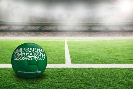 Football in brightly lit outdoor stadium with painted flag of Saudi Arabia. Focus on foreground and soccer ball with shallow depth of field on background and copy space.の写真素材