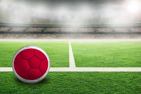 Football in brightly lit outdoor stadium with painted flag of Japan. Focus on foreground and soccer ball with shallow depth of field on background and copy space.の写真素材