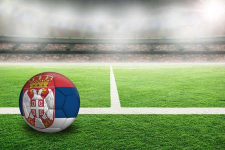 Football in brightly lit outdoor stadium with painted flag of Serbia. Focus on foreground and soccer ball with shallow depth of field on background and copy space.の写真素材