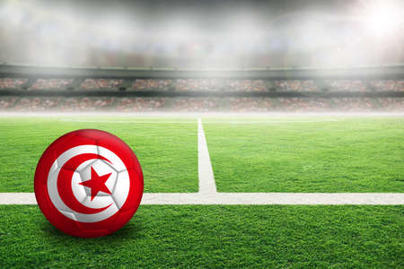 Football in brightly lit outdoor stadium with painted flag of Tunisia. Focus on foreground and soccer ball with shallow depth of field on background and copy space.の写真素材
