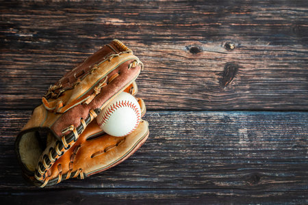 Leather baseball or softball glove with ball on rustic wooden background with copy space.