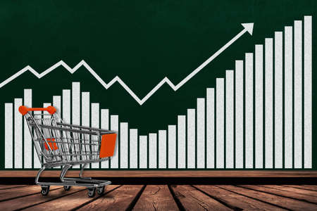 Shopping cart and growth chart on chalkboard with copy space. Concept of increases in sales, revenues, profits, economy, inflation, business activity.の写真素材