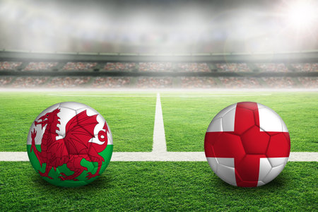 Wales vs England football in brightly lit outdoor stadium with painted English and Welsh flags. Focus on foreground and soccer ball with shallow depth of field on background and copy space.の写真素材