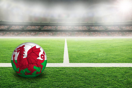 Wales football in brightly lit outdoor stadium with painted Welsh flags. Focus on foreground and soccer ball with shallow depth of field on background and copy space.の写真素材