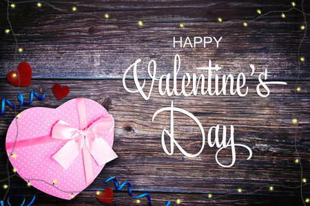 Happy Valentine's Day background with pink gift box, hearts, ribbons and string lights on rustic table flat lay.の写真素材