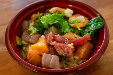 Hawaiian seafood poke bowl with diced salmon, tuna, shrimp; and salad isolated on wooden table background.の写真素材