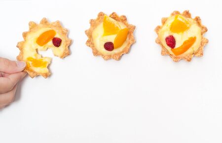 Berry, orange and apricot delicious cream tart. One of the tarts is torn apart by a hand.の写真素材