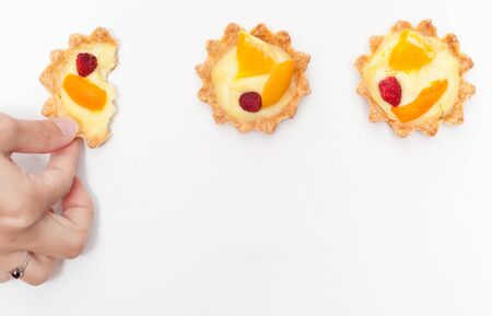 Berry, orange and apricot delicious cream tart. One of the tarts is torn apart by a hand.の写真素材