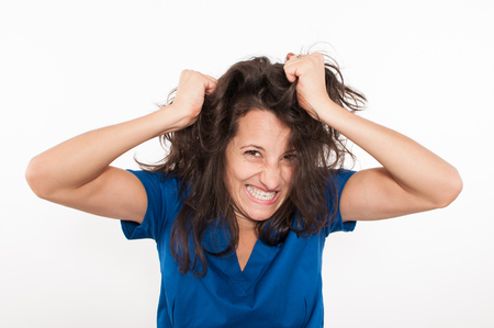 Angry young female doctor in blue coat pulling her hairの写真素材