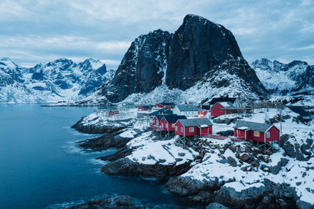 Red cabins in a snowy Norwegian village nestled by the sea and mountains..