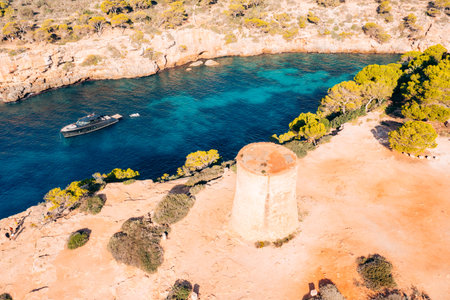 Tourists explore a historic tower and a luxury yacht anchors in a Majorca coveの写真素材