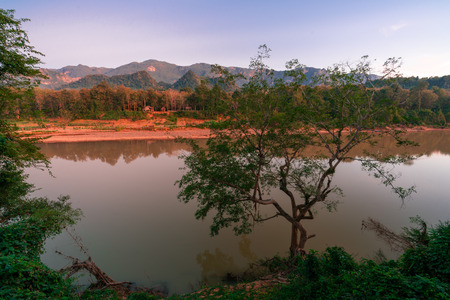 Sunset outside Luang Prabang. Sun shins on an old village. Jungle around the village. Nam khan river infront of the old village. Beautiful lightens up the jungle. Mountains in the background.の写真素材