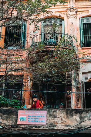 Hanoi, Vietnam, 12.20.18: Life in the street in Hanoi. Old lady on a balcony in an ancient buidlingのeditorial素材