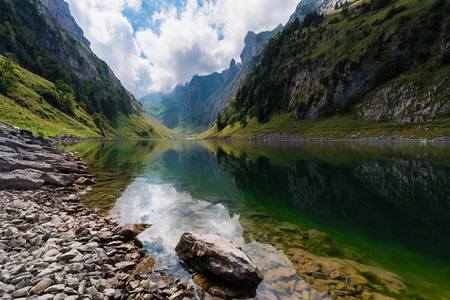 Mountain landscape in the Swiss Alps with jagged peaks and a pristine blue mountain lake in the valley far below.の写真素材